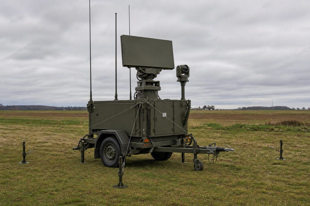 Aanhanger met een draaiend radarpaneel, een camerakop en dunne antennes in een weiland